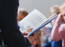 Aufgeschlagenes Buch. Im Hintergrund sind unscharf Kinder zu erkennen.